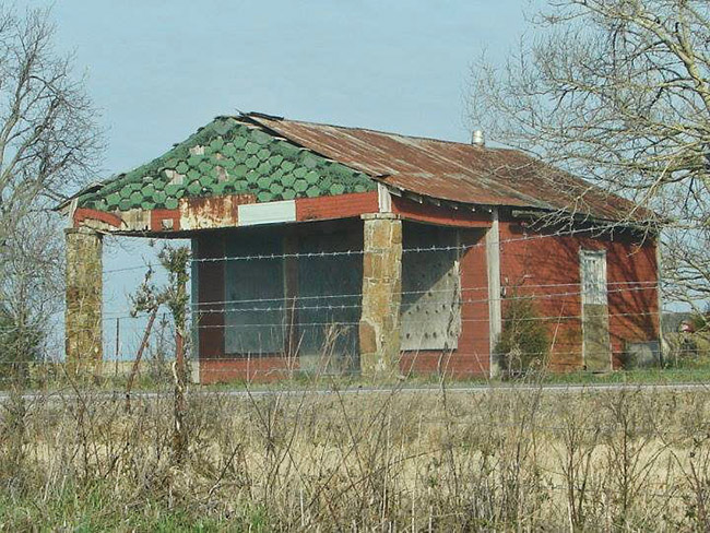 Abandoned building with dilapidated roof boarded-up windows and covered green entrance taken inside barbed wire fence