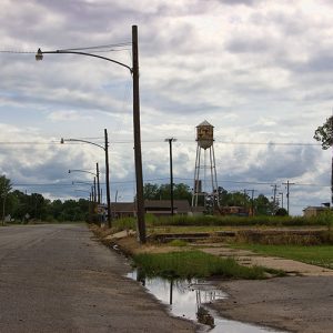 Rural road with street lamps on its right side and water tower next to single-story building in the background
