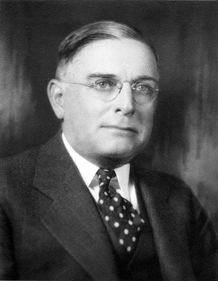 White man with glasses in suit with spotted tie