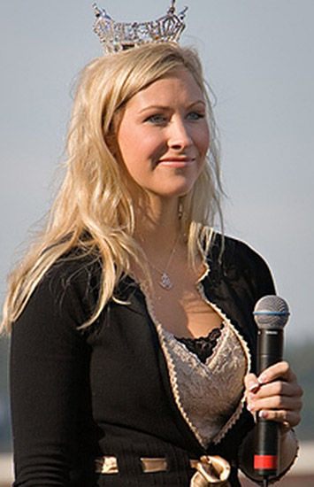 Young white woman with long blonde hair and crown holding a microphone
