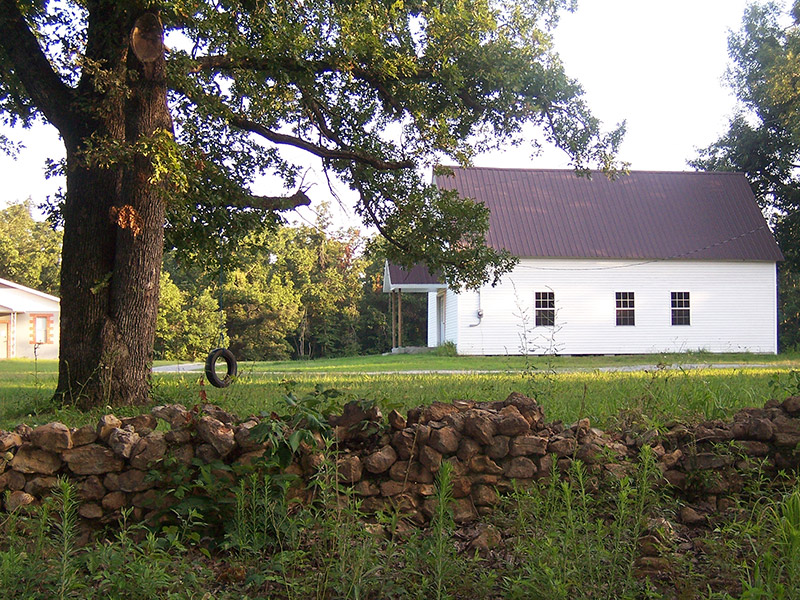 Side view of single-story building with A-frame roof and covered entrance with tree and tire swing in the foreground