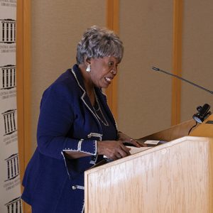 Older African-American woman in blue suit speaking at lectern