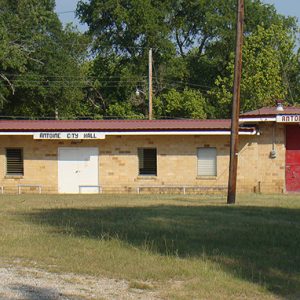 Single-story brick building with garage on grass with signs saying 'Antoine City Hall" and "Antoine Fire Dept."