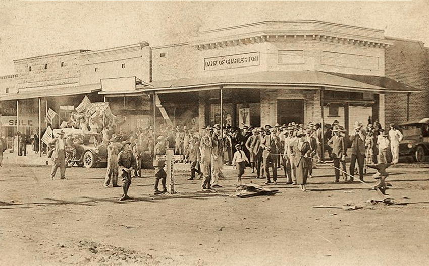 Large crowd of people standing on street with storefronts in the background