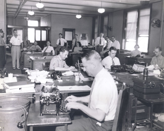 Room full of white men and women working on their typewriters