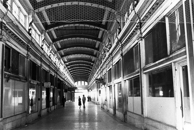 Arched hallway with rows of shops and signs with customers