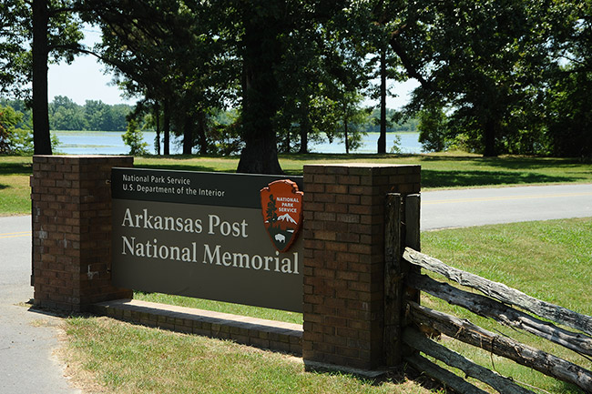 "Arkansas Post National Memorial" sign with trees and river