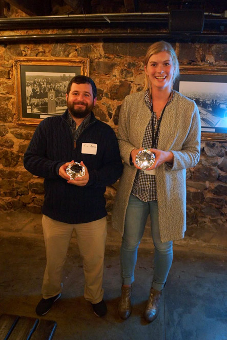 White man with beard smiling with award standing next to white woman in long coat smiling with award