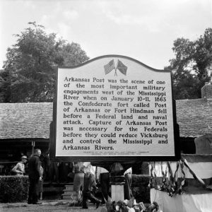 Historical marker in foreground with building and group of people in background