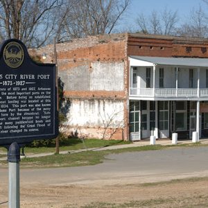 "Arkansas City River Port" historical marker sign on street corner with two-story building behind it