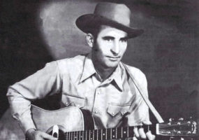 White men with hat in western clothing playing an acoustic guitar