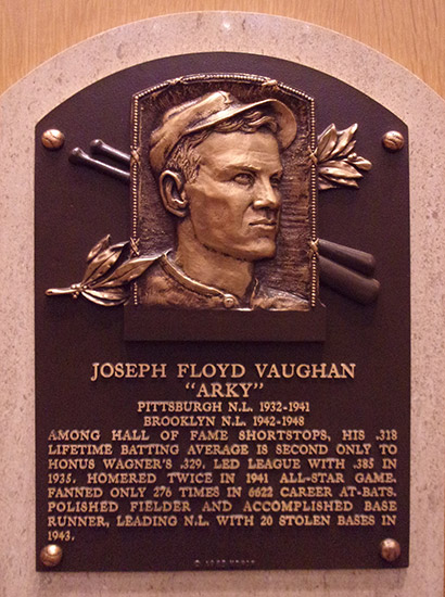 Bust of white man in baseball cap with bats and leaves on plaque with text