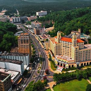 aerial view of downtown Hot Springs featuring the large somewhat triangular shaped Arlington hotel and various other tall buildings and boulevard with cars amid tree-covered hills