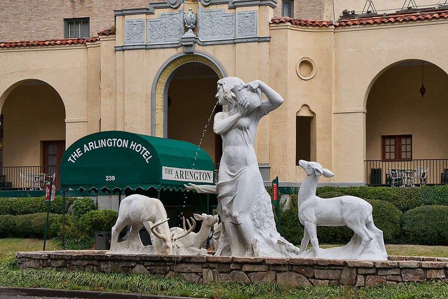 Fountain with statue of woman and deer outside multistory hotel with green awning over the entrance