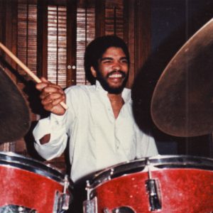 smiling younger African-American man with mustache and beard playing drums