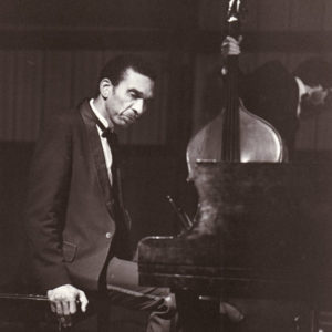 African-American man in suit sitting at a piano while another holds a stand-up bass