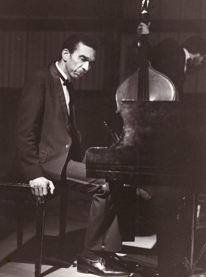 African-American man in suit sitting at a piano while another holds a stand-up bass
