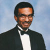 African-American man with mustache wearing large glasses in tuxedo and bow tie