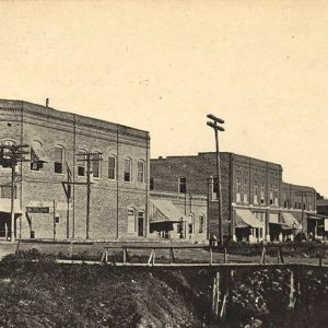 Foot bridge over creek with two-story brick buildings and corner store on street