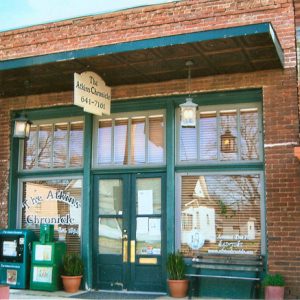 brick store front with teal painted wood trim with lanterns hanging "The Atkins Chronicle"