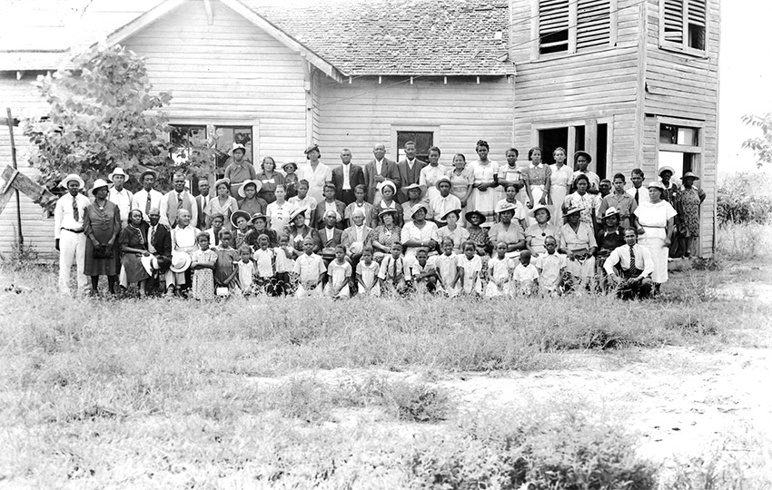 Group of African American men women and children posing in front of wooden church building
