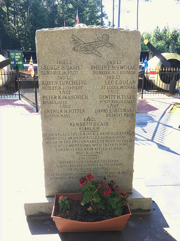 Stone monument with engraving of airplane in flight and text with names and flower bed at its base