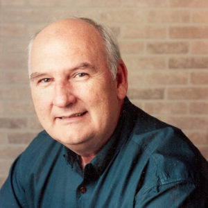 portrait photo of white man in green shirt with brick wall behind him