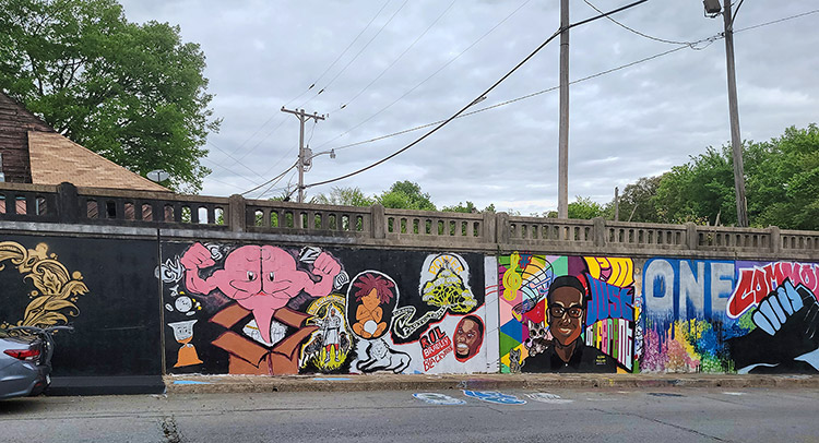 Anthropomorphic brain busting from cardboard box and African-American figures painted on concrete viaduct wall with railing