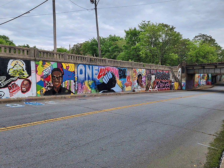 African-American figures and clasped hands with "One Common Goal" painted above them on concrete viaduct wall on two-lane road