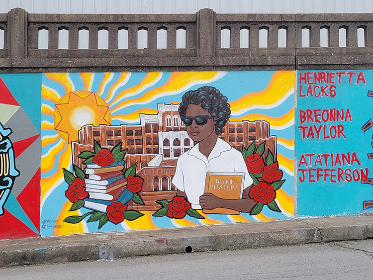 African-American girl holding "Black History" book with stack of books on her left side and roses with multistory school building behind her painted on concrete wall