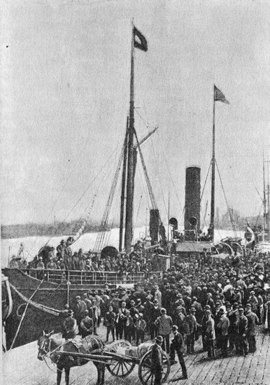 Crowd of people gathered at boat dock and aboard a ship with horse-drawn cart in the foreground