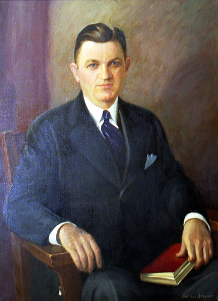 White man wearing a suit and tie sitting in a wooden chair