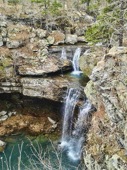 Natural waterfall over rock face leading to a pool below