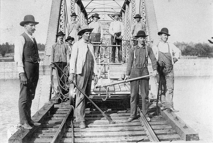 White men with hats and tools and push cart on steel truss bridge