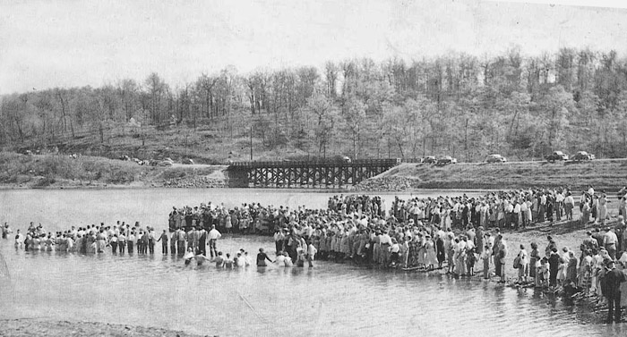 Crowd of people standing in or near a river with bridge in the background