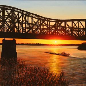 Steel truss bridge over river with barge passing under it at sunset