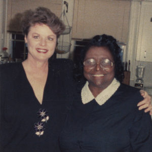 White woman smiling in dress next to African-American woman with glasses smiling in dress