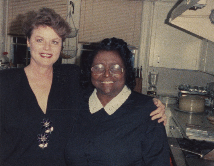 White woman smiling in dress next to African-American woman with glasses smiling in dress