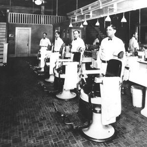 Row of white men standing next to empty barber chairs