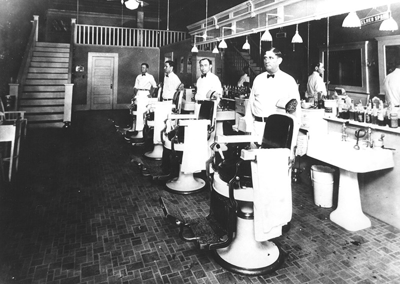 Row of white men standing next to empty barber chairs