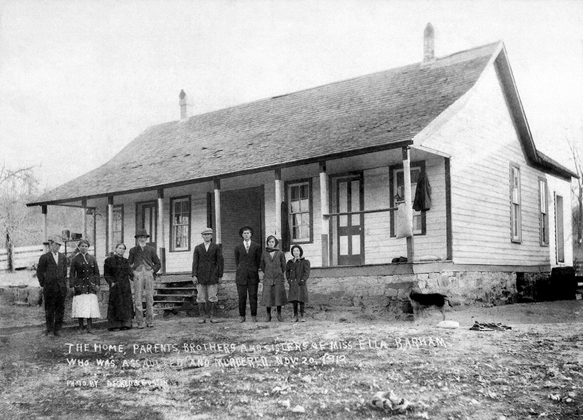 White men women and girls standing outside single-story house with covered porch and slanted roof