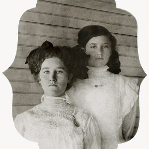 Two young white women in white dresses standing against building with wooden siding