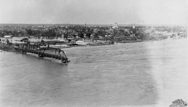 part of a bridge extending into a river with flooded city in background