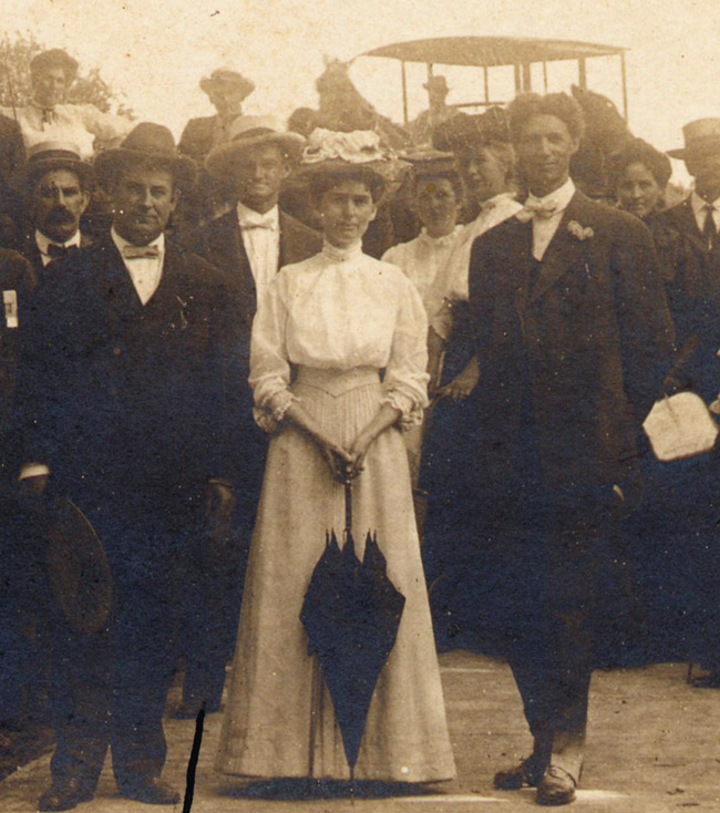 Crowd of white men and women in formal dress with horse drawn carriage behind them