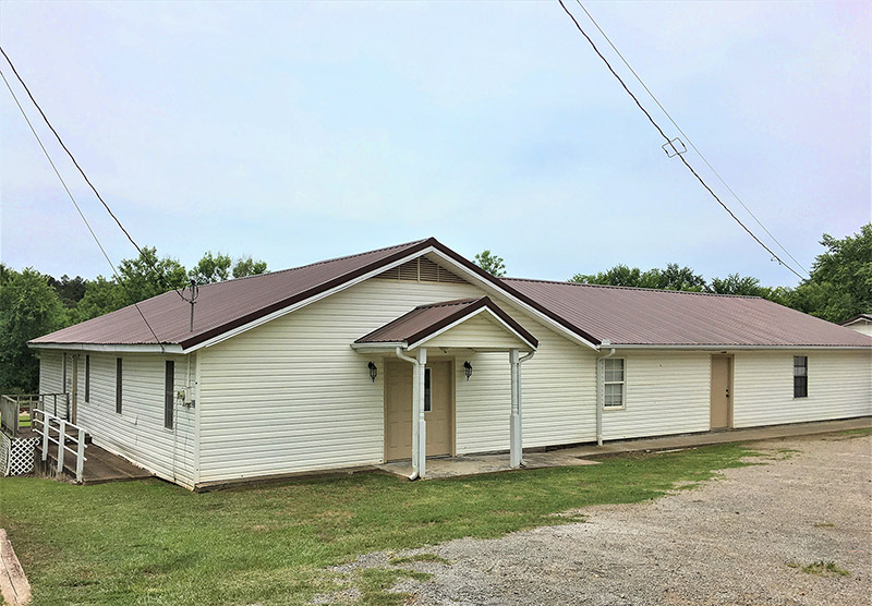 Single-story building with siding and covered porch on gravel parking lot