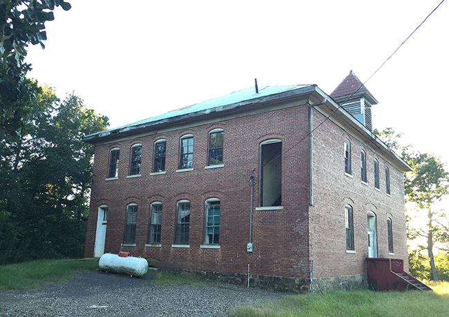 Side view of two-story brick school building with propane tank next to it and cupola on the roof