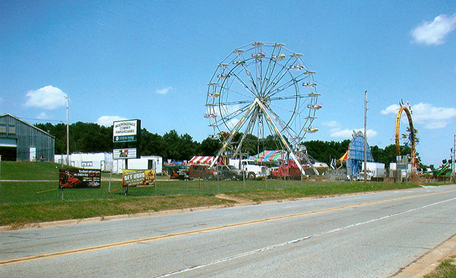 Street with metal building next to carnival rides with Ferris wheel and loop roller coaster