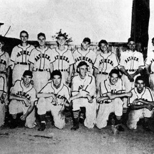 Group of young white men in baseball uniforms posing on field