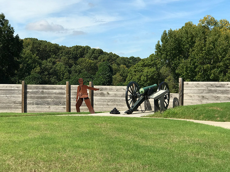 Fort walls and cannon with stack of balls next to it and metal representation of a soldier