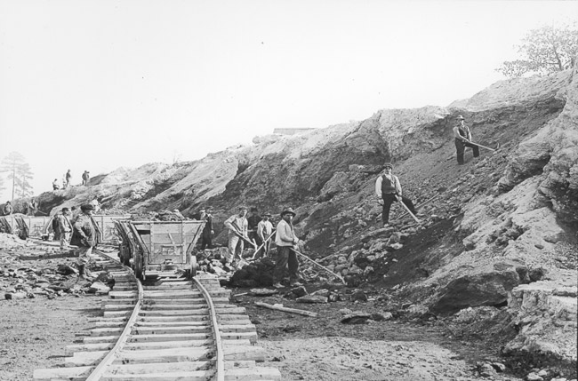 White miners filling small rail cars on a track with bauxite ore